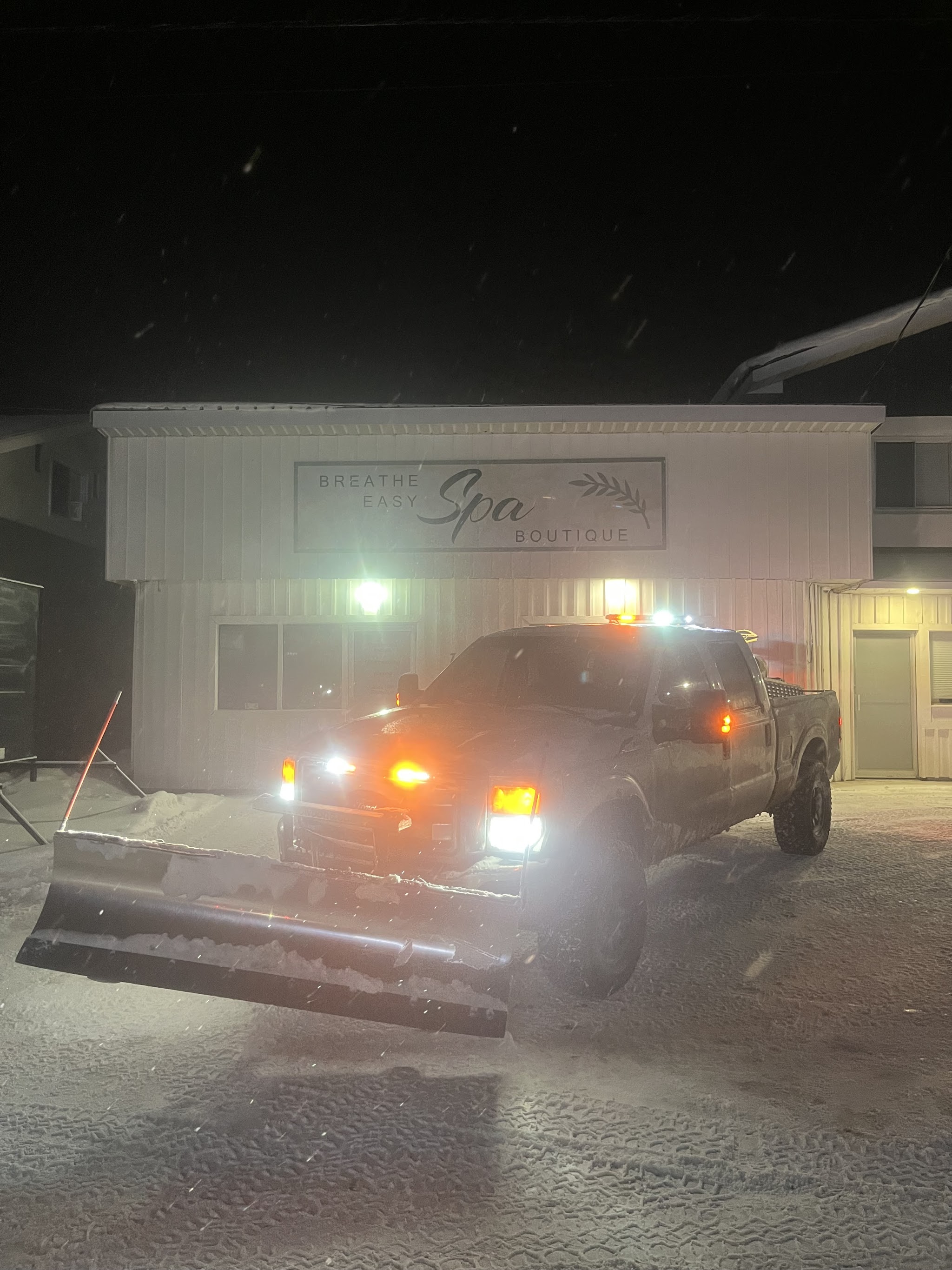 Snow plow truck clearing a commercial driveway at night